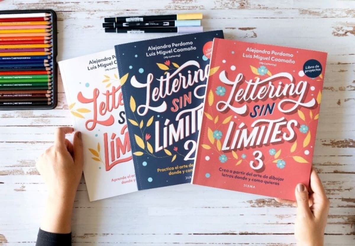 The three Lettering sin límites books held over a worktable next to markers and colored pencils